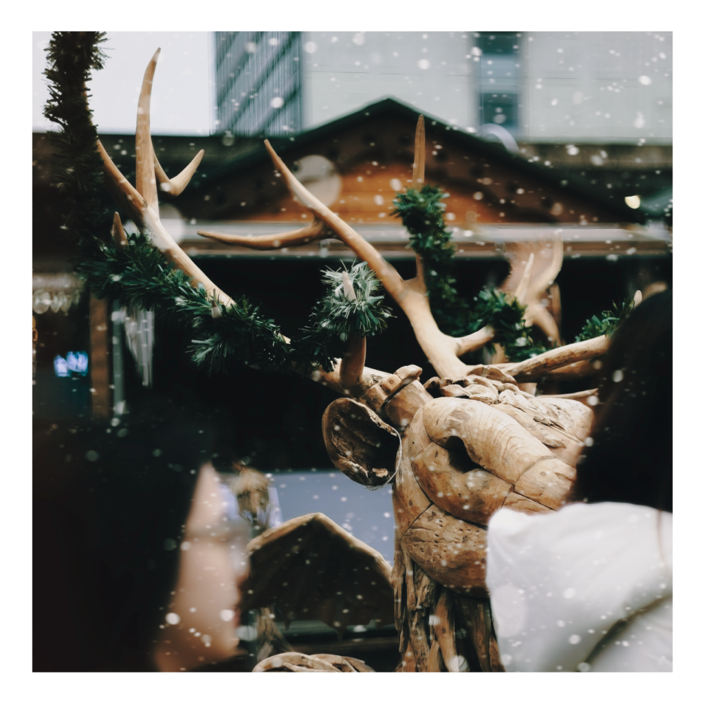 Decorative reindeer ornaments arranged among evergreen branches in a Christmas display, photographed with warm, soft lighting creating a festive holiday scene.