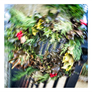 Abstract photograph of a Christmas wreath created using intentional camera movement, showing swirling green foliage with red berries in a circular motion blur pattern that creates a vortex effect.