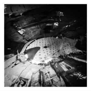 Black and white photograph looking up at the curved mirrored ceiling at Manchester Central Library entrance, showing warped reflections creating abstract geometric patterns with polka-dot details.