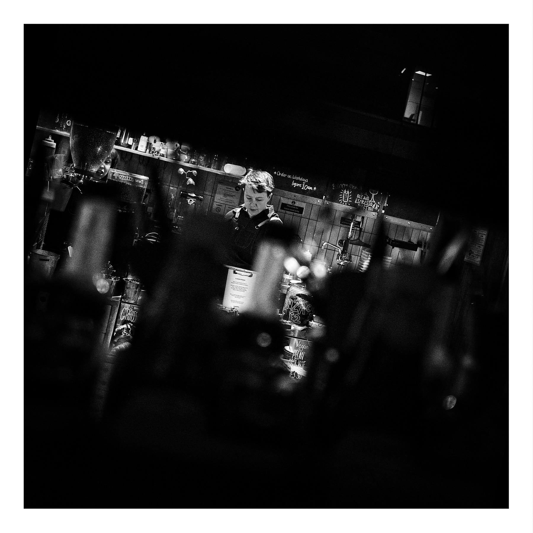 Black and white photograph of staff setting up at Federal cafe bar on Oxford Road Manchester, shot through the window with bottles and cutlery creating a natural frame in the foreground.