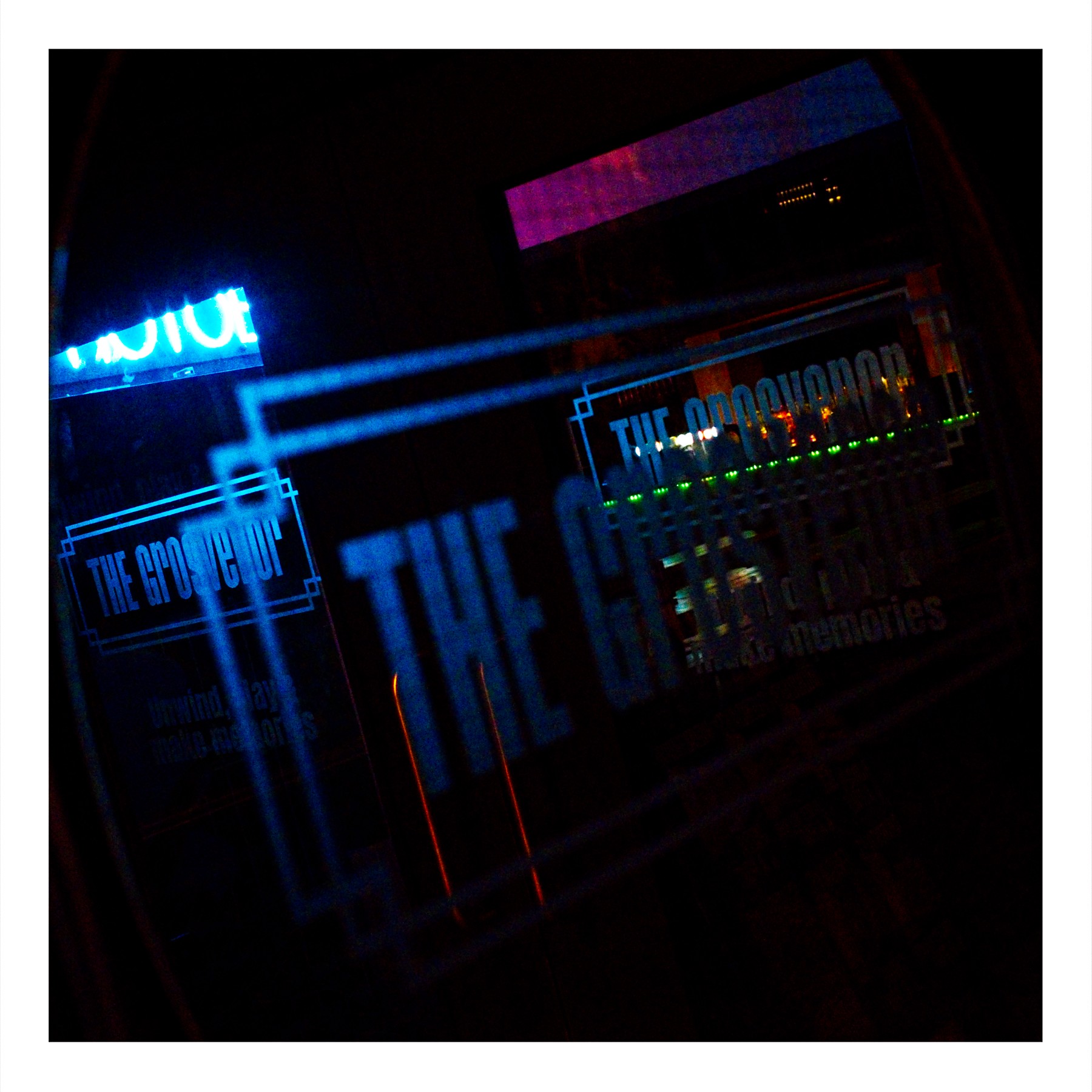 Nighttime photograph showing multiple glass doorway reflections of The Grosvenor nightspot on Oxford Road Manchester, with vibrant blue, pink and green neon lighting creating layered reflections.